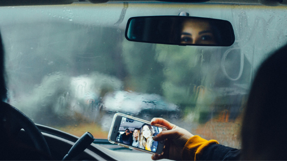 Photo of auto interior, with a person taking a photo on a mobile phone -- Distracted Driving Mason McBride Insurance Michigan
