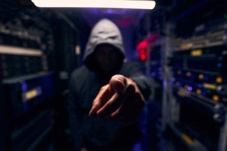 mysterious figure wearing a hoodie and pointing towards the concept of cyber attack insurance.