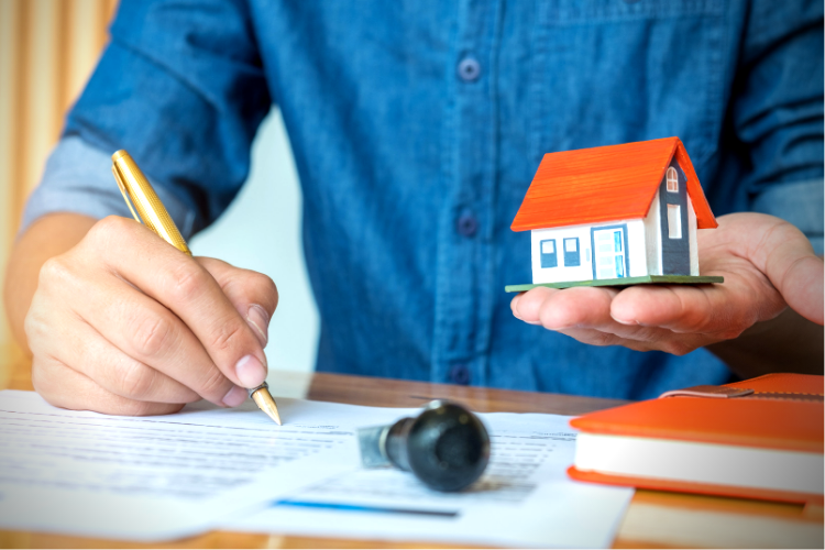 insurance-to-value replacement cost. Picture of man holding a small house with paperwork in front of him.
