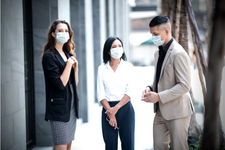 three working professionals gathered outside on sidewalk wearing masks