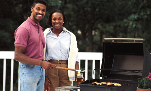 Photo of a young couple on a deck using a barbeque grill.