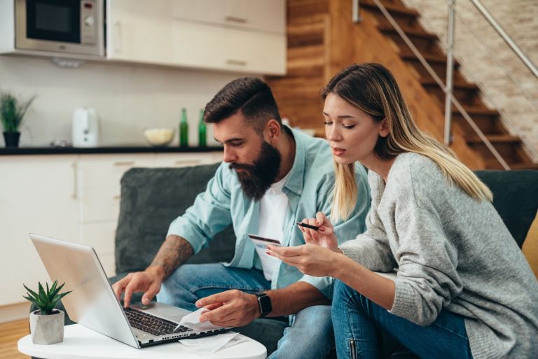 Couple sitting on a couch, working on their monthly bills, including home and auto insurance.